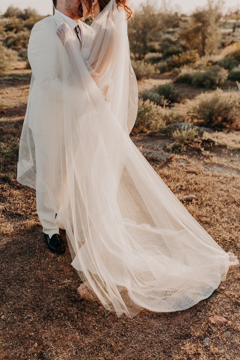 bride and groom snuggle in the desert at sunset