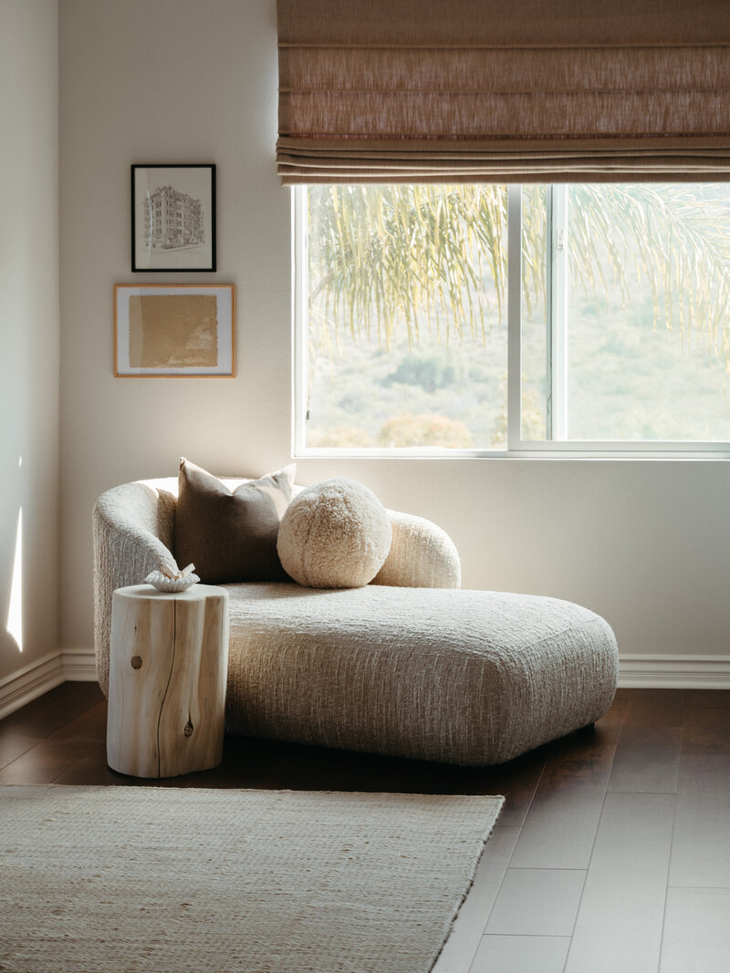Sunlit reading nook featuring a modern boucle chaise lounge, neutral-toned pillows, and a natural wood stump side table in a serene San Diego interior.