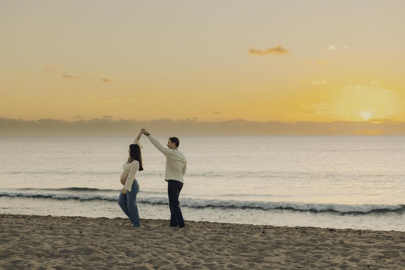 couple dances on beach during maternity photos