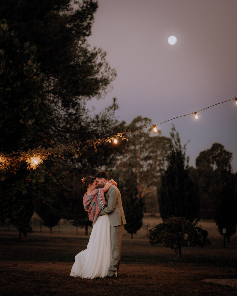 Bride & Groom dancing under string lights as the moon rises behind them