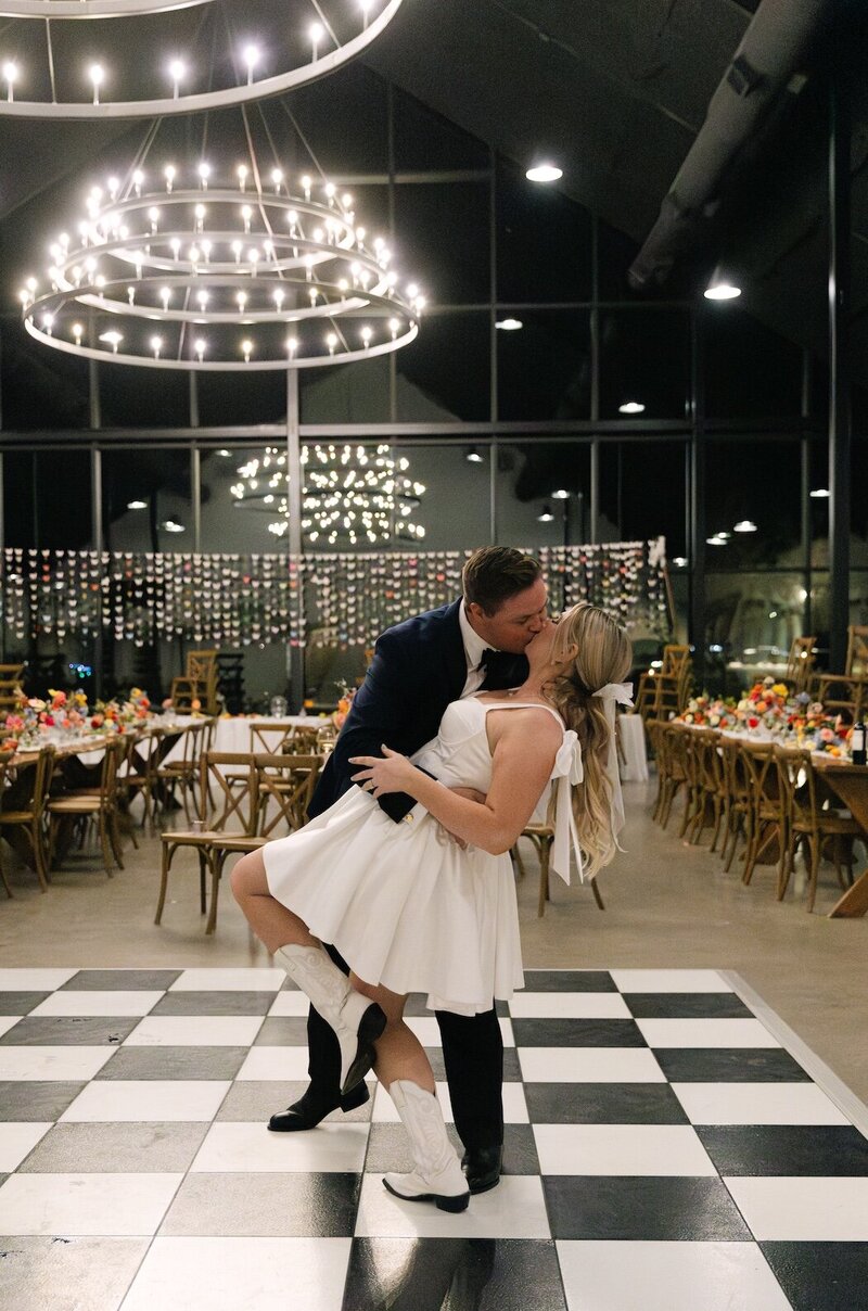 Bride and groom sharing a dance on black-and-white checkered floor beneath modern chandeliers at Camp Hosea wedding reception.