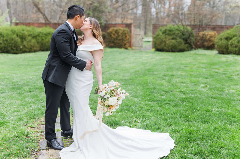 A man and woman kiss at an Estate in Cincinnati. She is wearing her bridal gown and he is wearing a black tux.