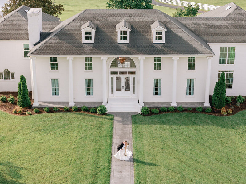 Aerial photo of a bride and groom kissing in front of wedding venue 