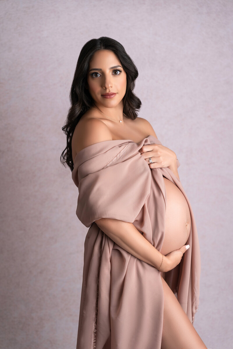 pregnant  mother-to-be  posing outside in a flowy pink dress holding her pregnant belly