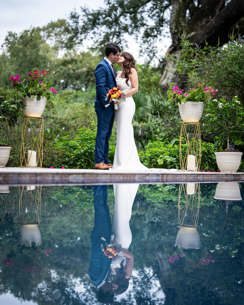 Bride and groom kissing with reflection in pool at upscale Metairie residence