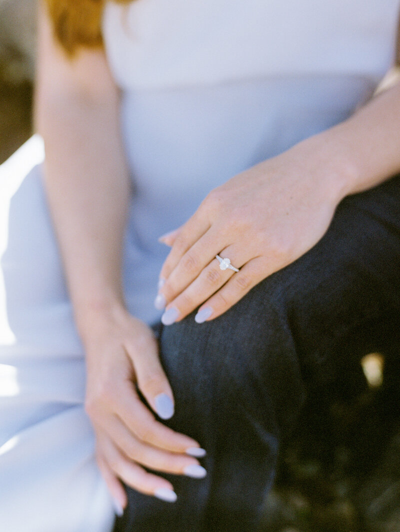 a woman in a purple dress with her hands on a mans leg showing an oval cut diamond ring and purple nails