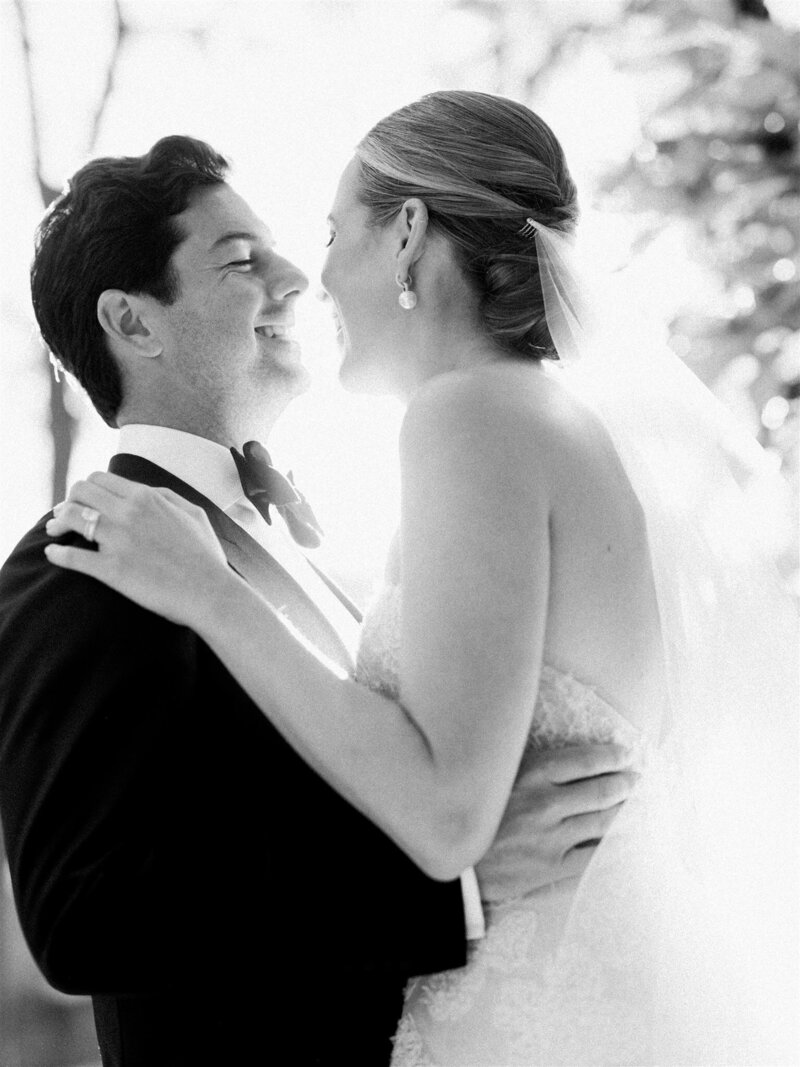 Black and white photo of a bride and groom gazing into each other's eyes, with the bride's veil softly framing her face.