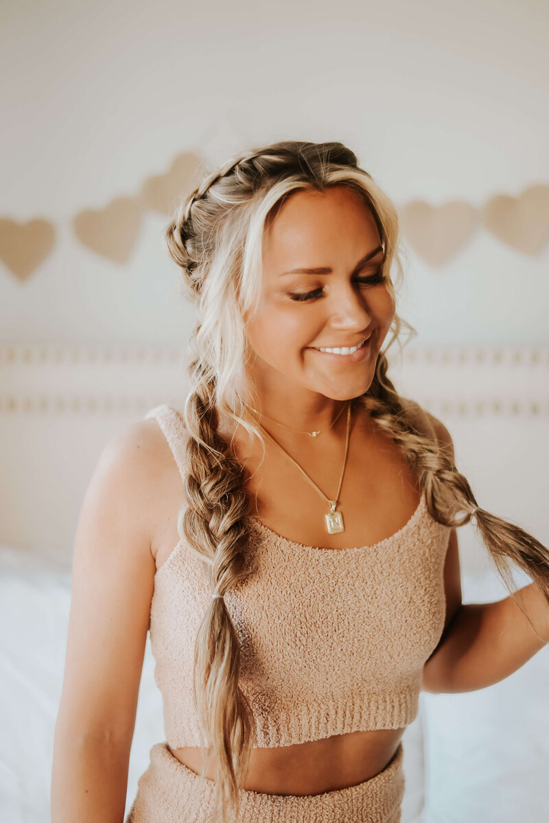 Woman wearing peach tank top and braided hair smiling and looking at her hair