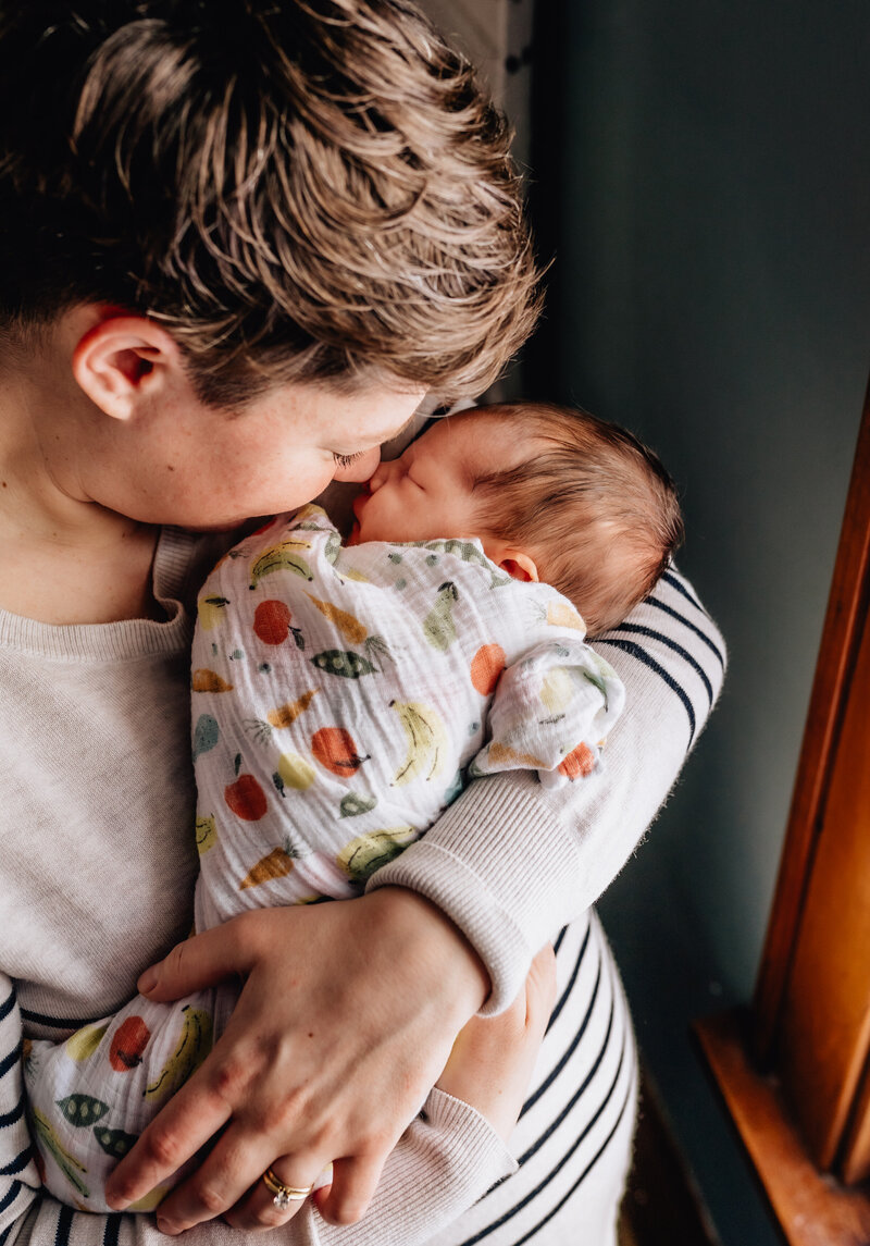 A close-up image of a person gently holding a swaddled newborn close to their face.