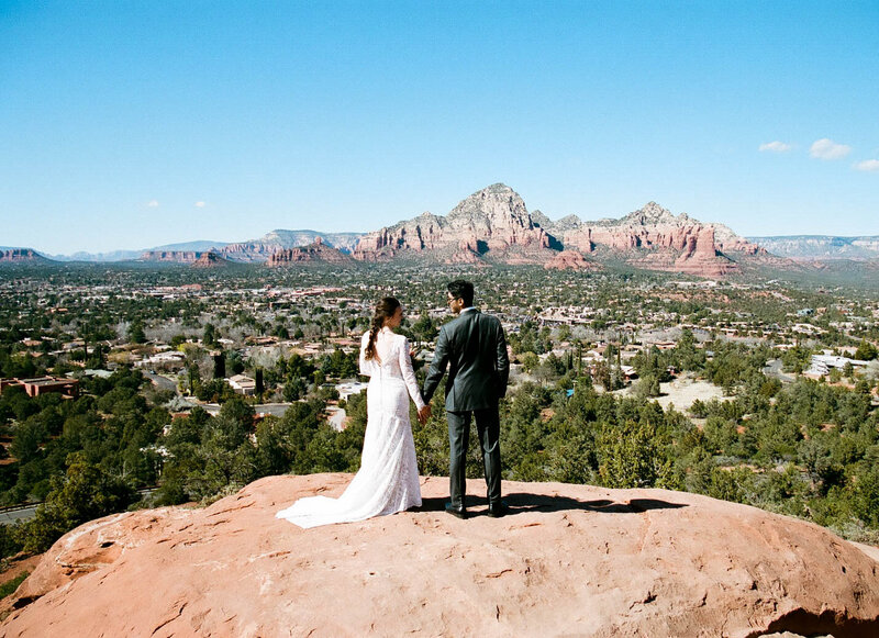 Bride and groom holding hands standing on top of a rock looking out at the sedona red rock mountain views