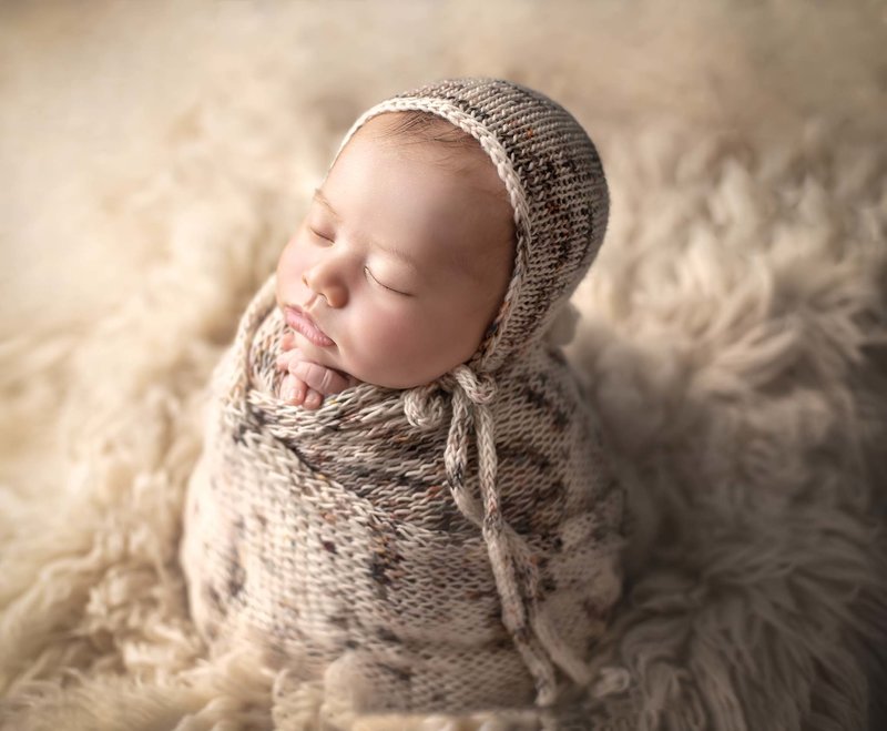  "Newborn baby peacefully sleeping, wrapped in a soft cream-colored fabric, captured in a serene and timeless pose during a fine art newborn photography session in Ottawa."