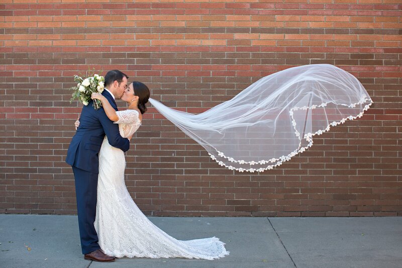 Bride and groom kiss as bride's veil blows in the wind