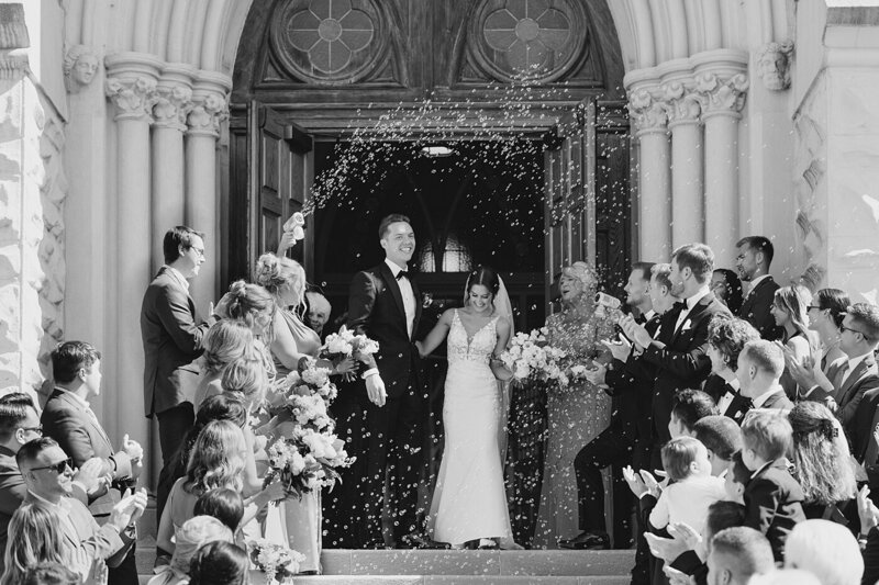 black and white wedding picture of bride and groom exited a chapel and their guests lined up to throw rise at them photographed by Columbus wedding photographer