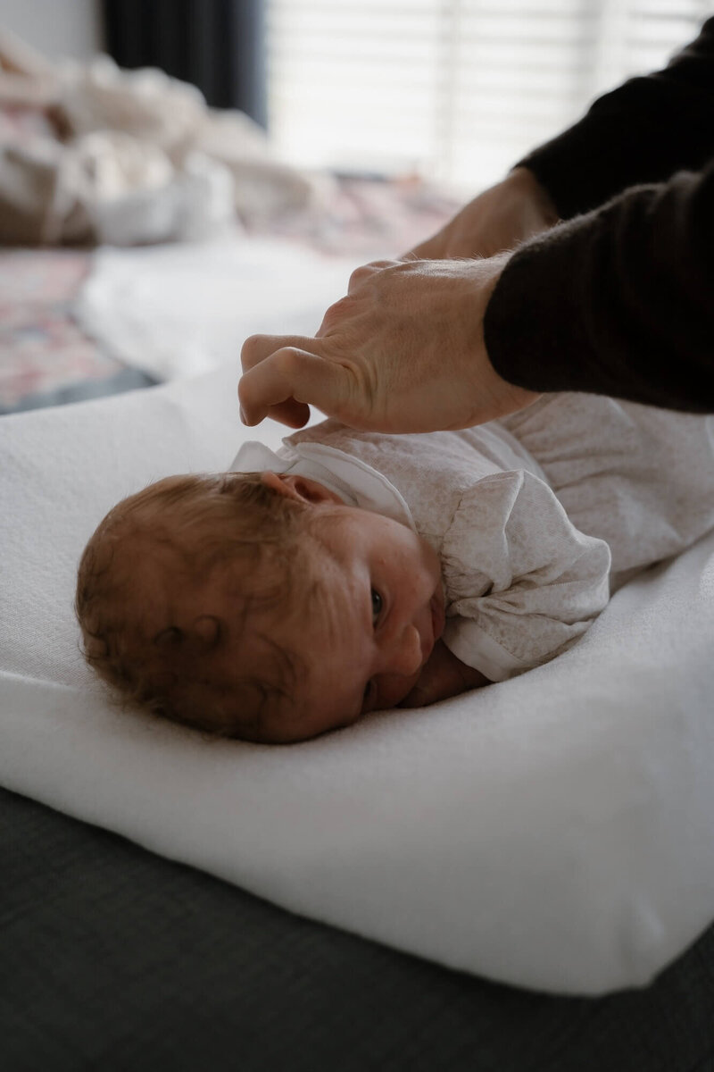Pasgeboren baby wordt gekleed tijdens newborn fotoshoot door fotograaf Julia de Groot