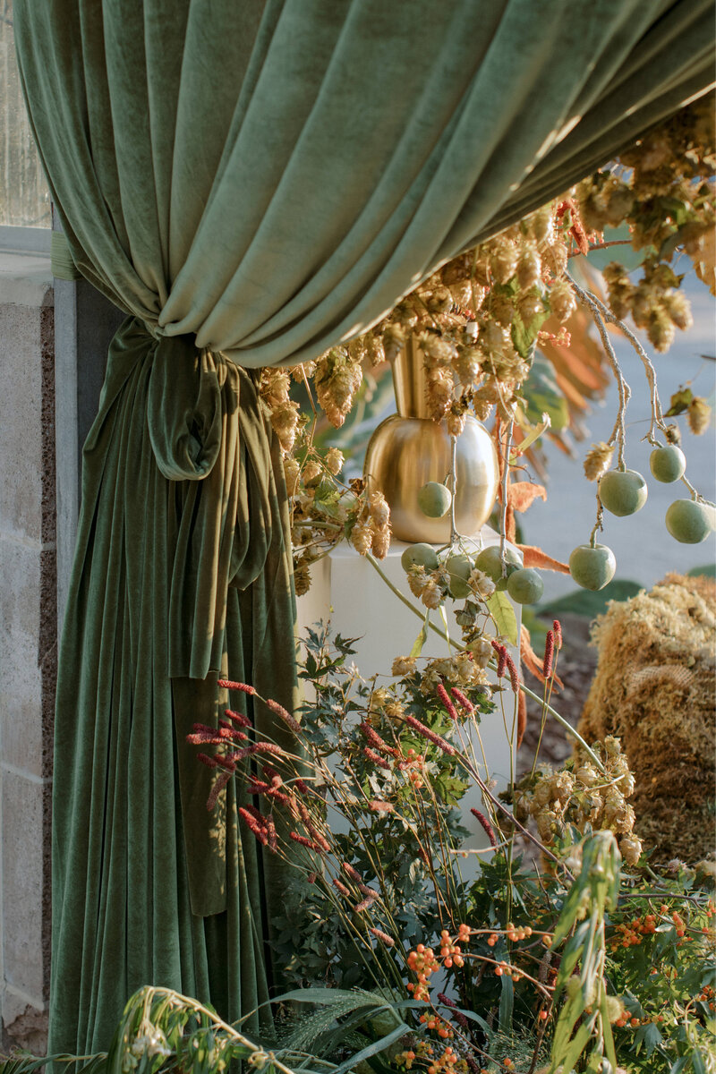 Grand green velvet curtain and lush floral installation at entrance of wedding reception space