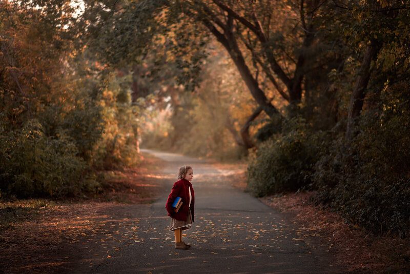 A beautiful fall backdrop with a little girl standing with a stack of books in her arms. Taken by Brittany Danielle Photography