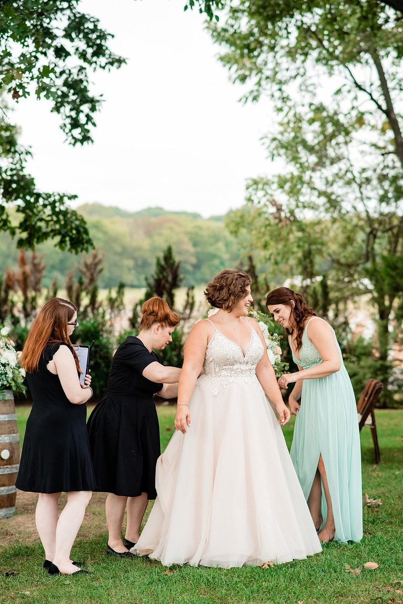 Outdoor photo of a bride surrounded by wedding planner team as they help bustle her wedding train