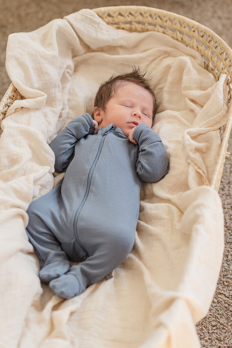 newborn baby boy in blue onsie sleeping on a cream blanket in a moses basket by lancaster pa photographer