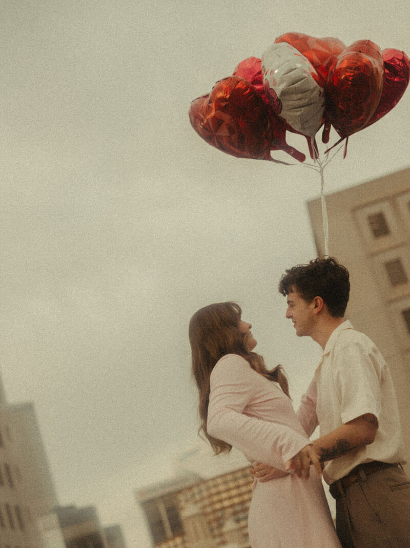 A couple standing close with balloons above them.