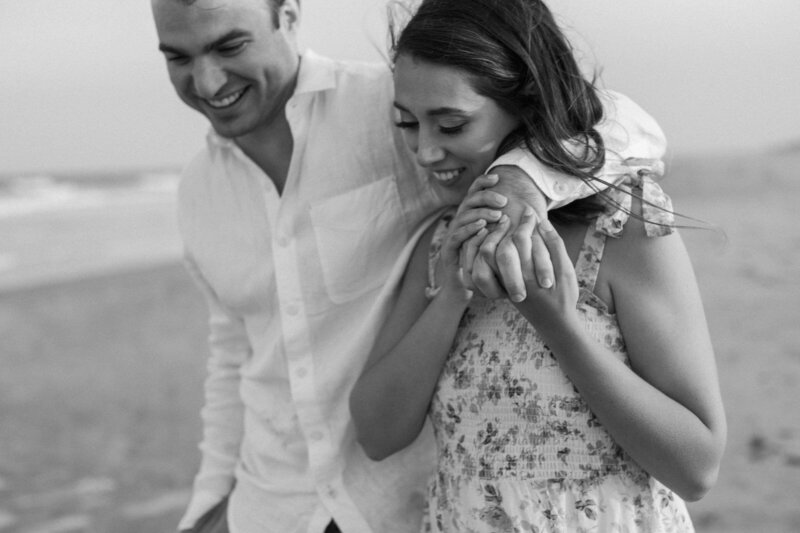 Wind blows through their hair as they run hand in hand along the shoreline, sand kicking up behind them