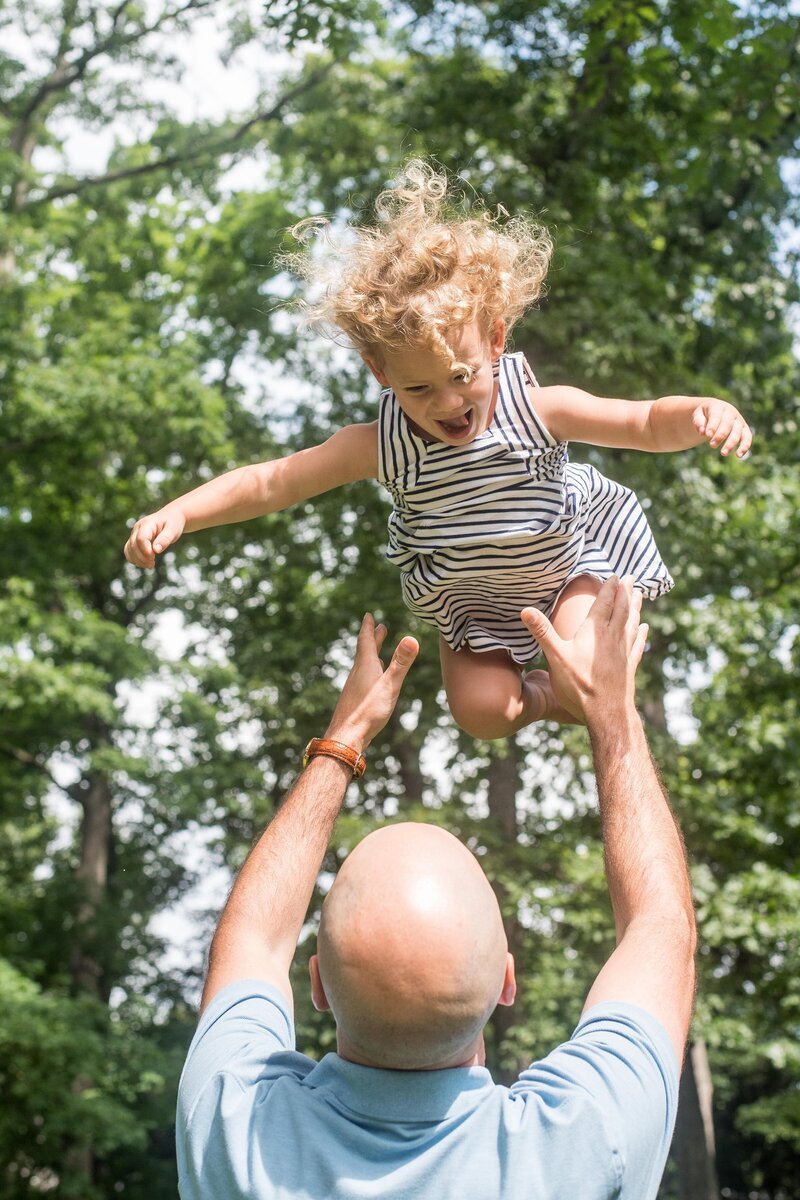 a father throws his laughing daughter into the air