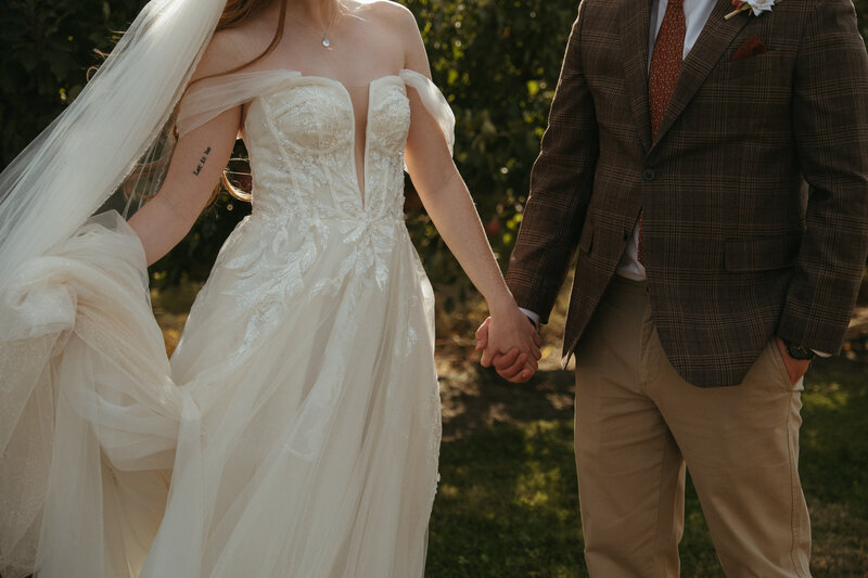 a couple holds hands together in a sun lit field after their wedding ceremony