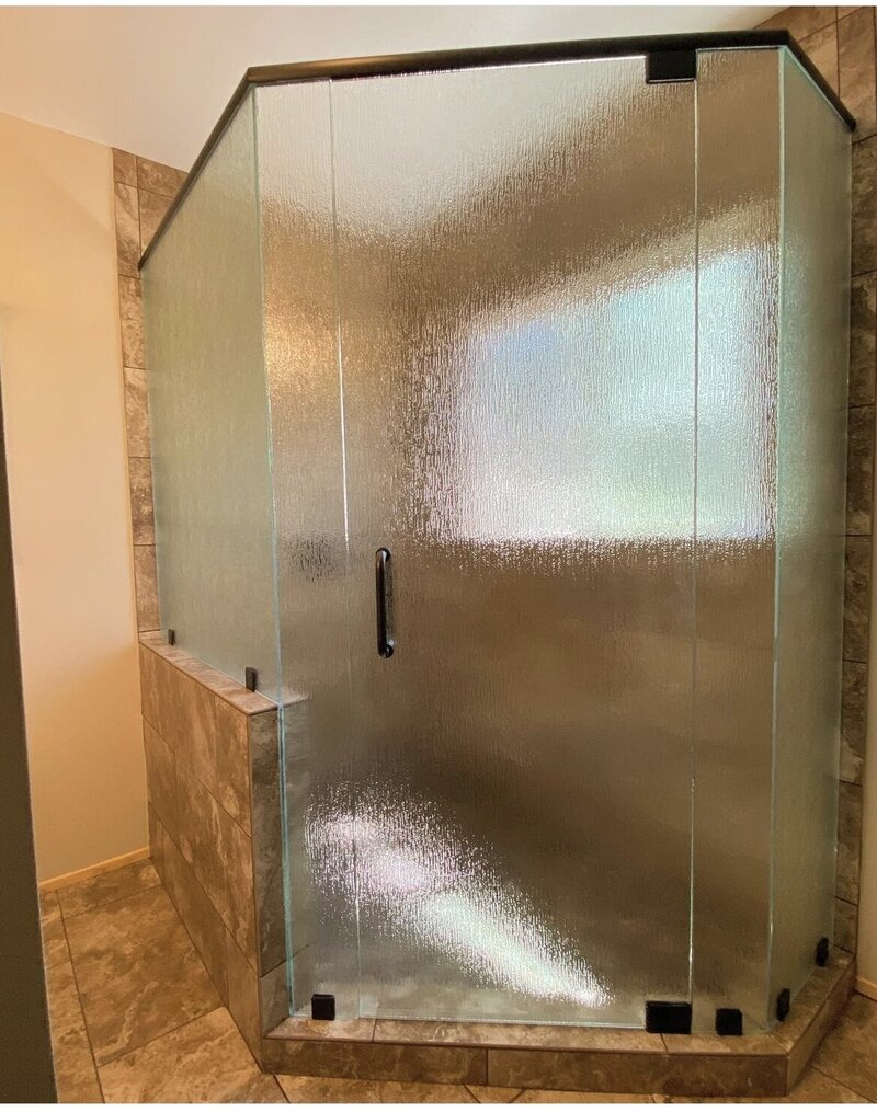 A remodeled shower with bronze hardware and obscure glass to create privacy. The doors of the shower are the same tile as the bathroom floors.