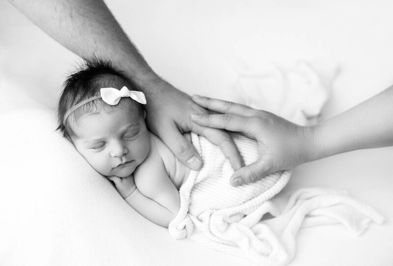 A baby is posed with mom and dad's hands for a maternity and newborn photographer in Coquitlam