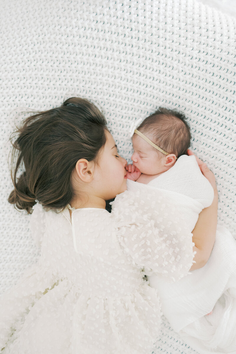 a young girl cuddling with her newborn sister