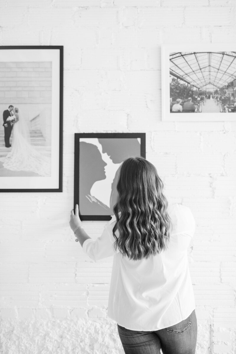woman hanging up printed wedding photos in frames on the wall
