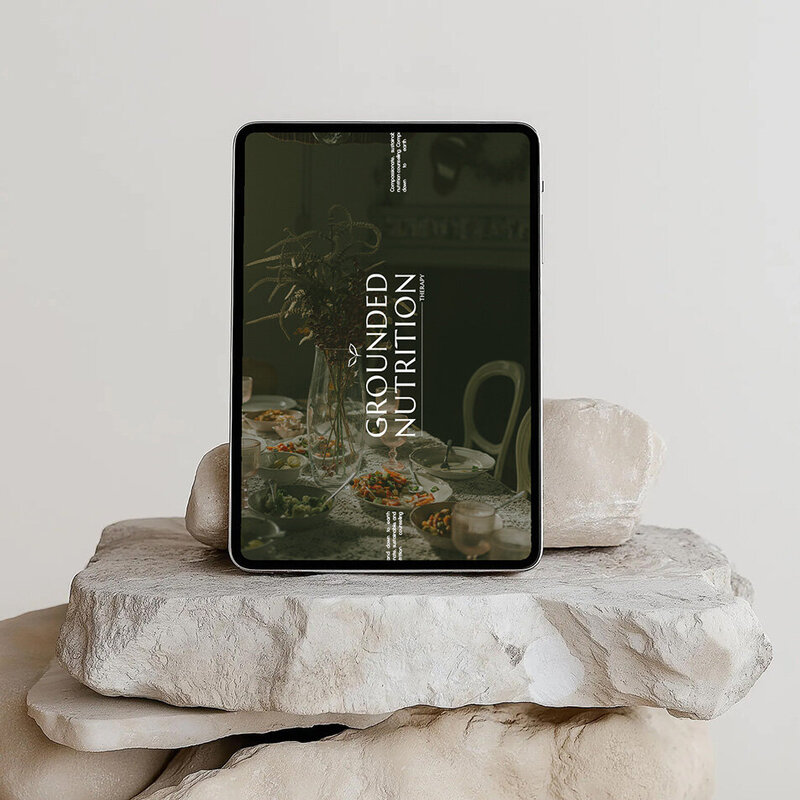 An iPad sitting on stacked rocks featuring nutritionist branding and elegant design elements.