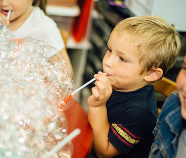 preschool boy blowing bubbles to create a bubble mountain inside of a bowl on a table