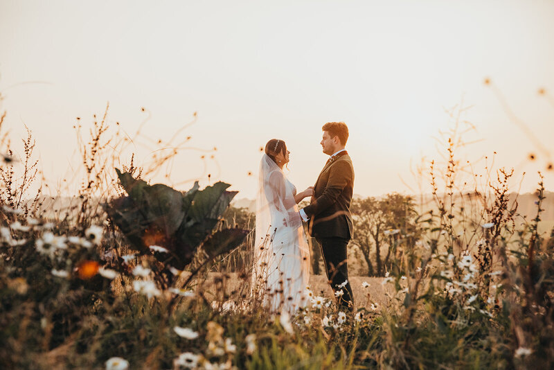 bride and groom hold hands in field during sunset