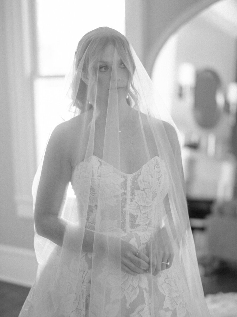 bride covered in her veil peering out the window