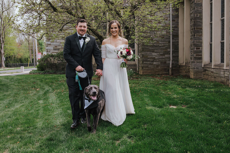 A couple smiles while standing with their dog.