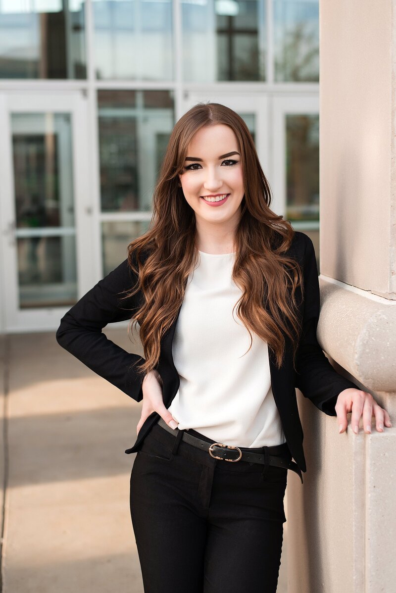 Girl wearing black slim fit suit and cream top smiling at camera with a power pose