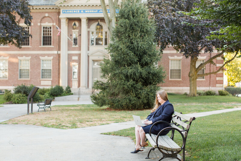 Monique sitting on bench outside courthouse with laptop