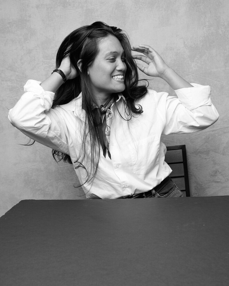 lack and white portrait of a woman laughing joyfully, running her hands through her hair as she looks to the side. She wears a crisp white button-up shirt, a stylish scarf, and high-waisted jeans, exuding confidence and energy. A lively, unfiltered moment from 'THIS IS ME – A Photography Experience by Katie Campbell' in Atlanta, GA, celebrating self-expression and authenticity.