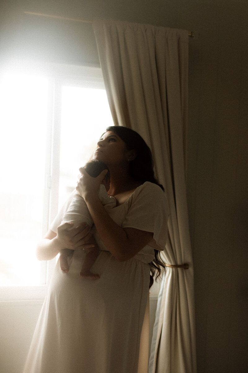 New mom holding her baby close, eyes closed, in a cozy in-home newborn session in Murrieta.