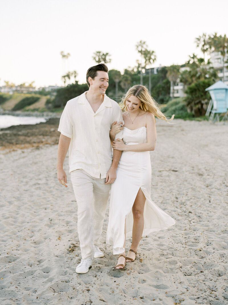 A woman and a man walk happily along the beach during their engagement session in San Luis Obispo