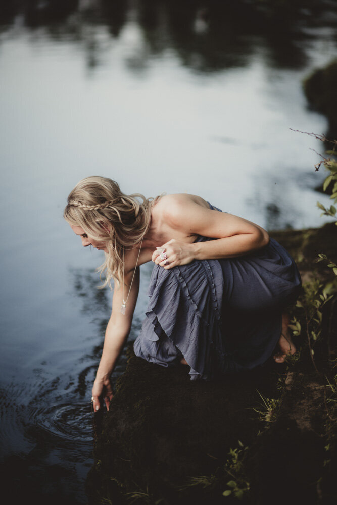 Caroline Weiss leaning over to touch calm water, symbolizing reflection, harmony, and soul wisdom.