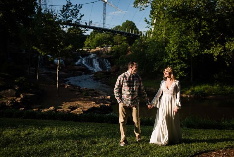 A newly engaged couple stand together holding hands with lush greenery in the background.