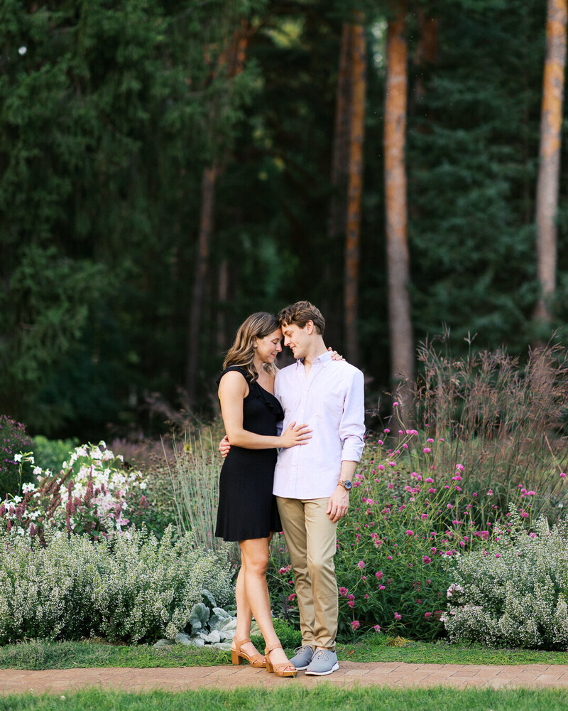Couple standing in the moment with heads resting together under tall trees in Wayzata Beach.