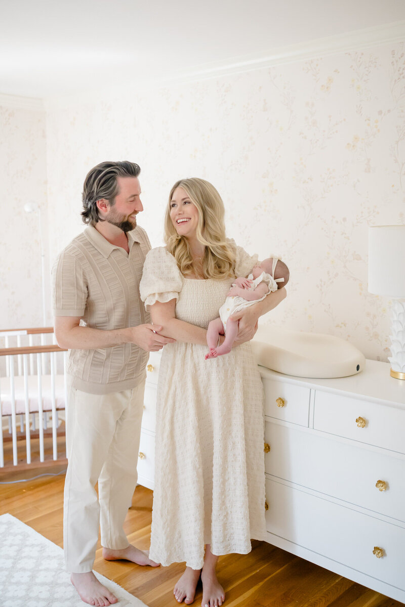 A new mother sits on her bed, cradling her swaddled newborn in a cozy in-home lifestyle session. She gently touches noses with her sleeping baby, sharing a tender moment filled with love and warmth