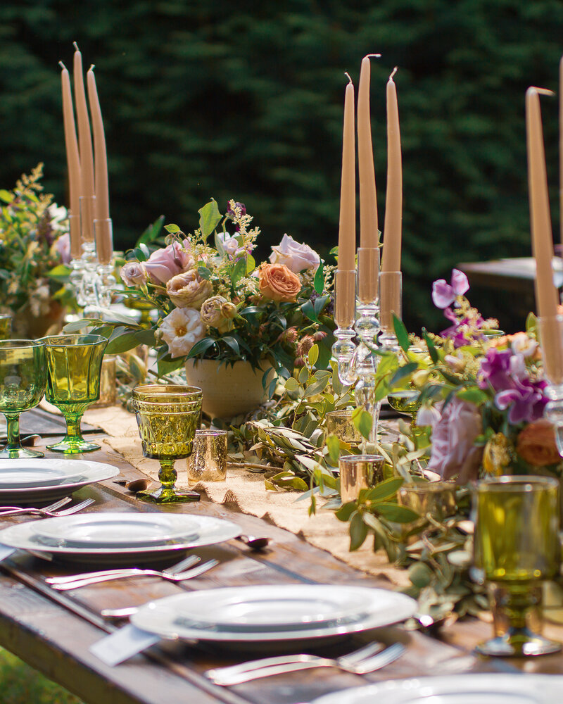 Rustic Wedding reception decor with  pink, peach, purple  and green floral centrepieces on a wooden table outdoors.