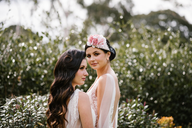 Two brides getting married, wearing white wedding dresses and pink floral headpiece