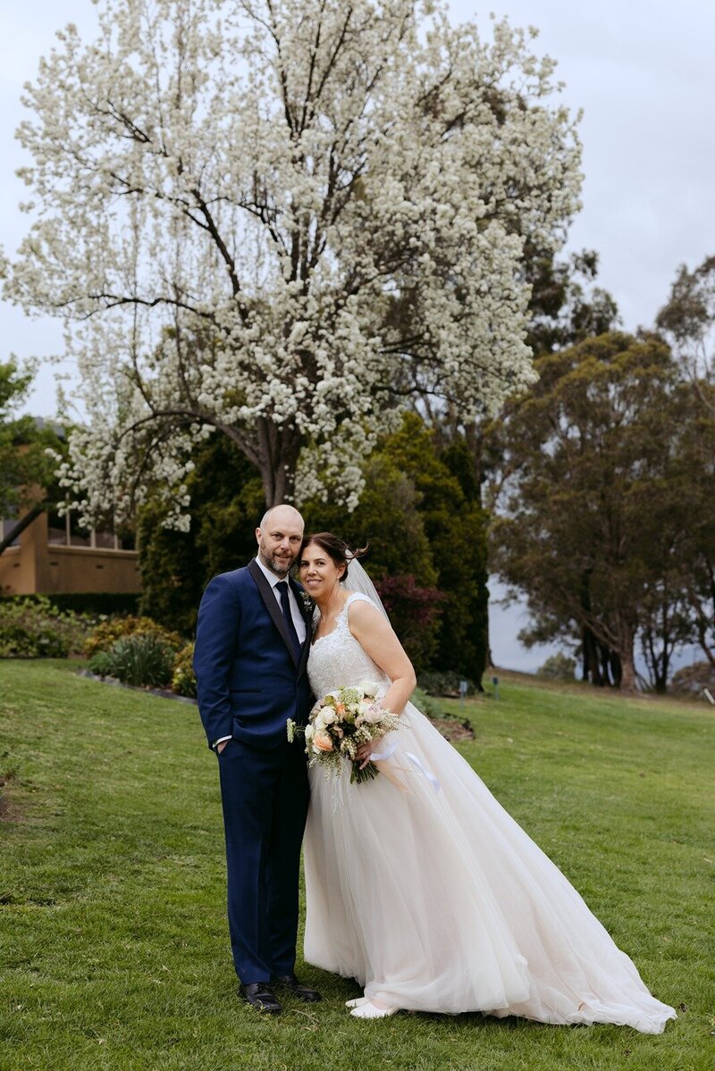 A bride and groom hugging at a floral alter on the ground in front of a wall of wine barrels.