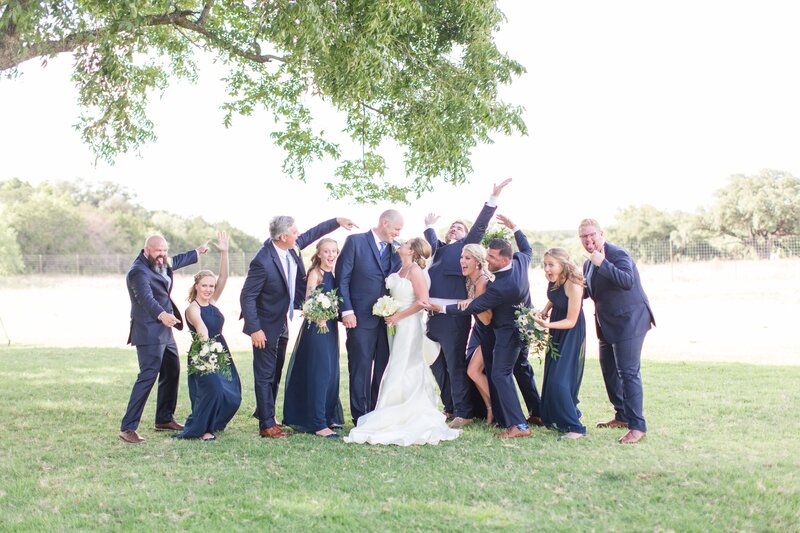 A wedding party joyfully surrounds the bride and groom in an outdoor setting, capturing the lively, fun-filled atmosphere of a Socially Significant Events wedding.