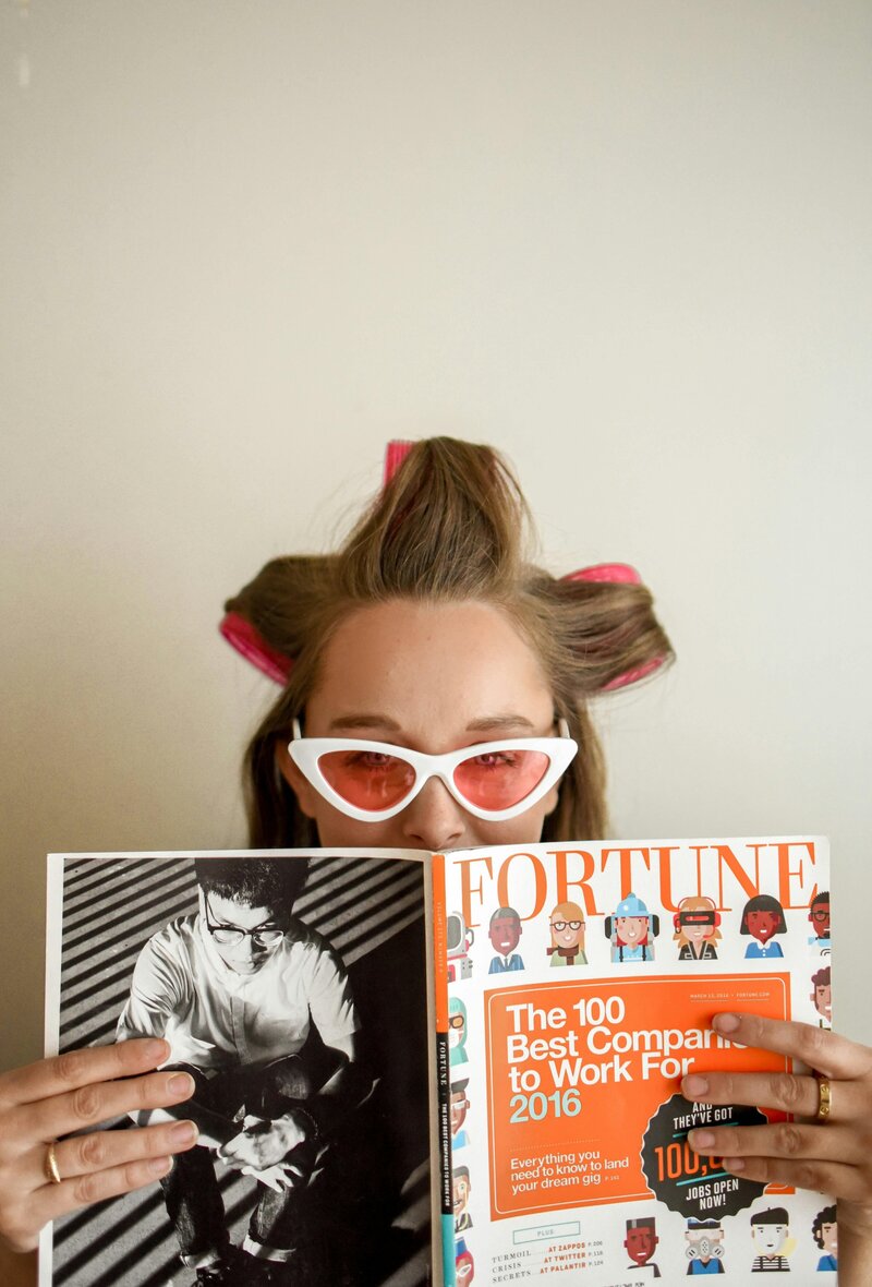 Lady in curlers and white glasses looks over a magazine