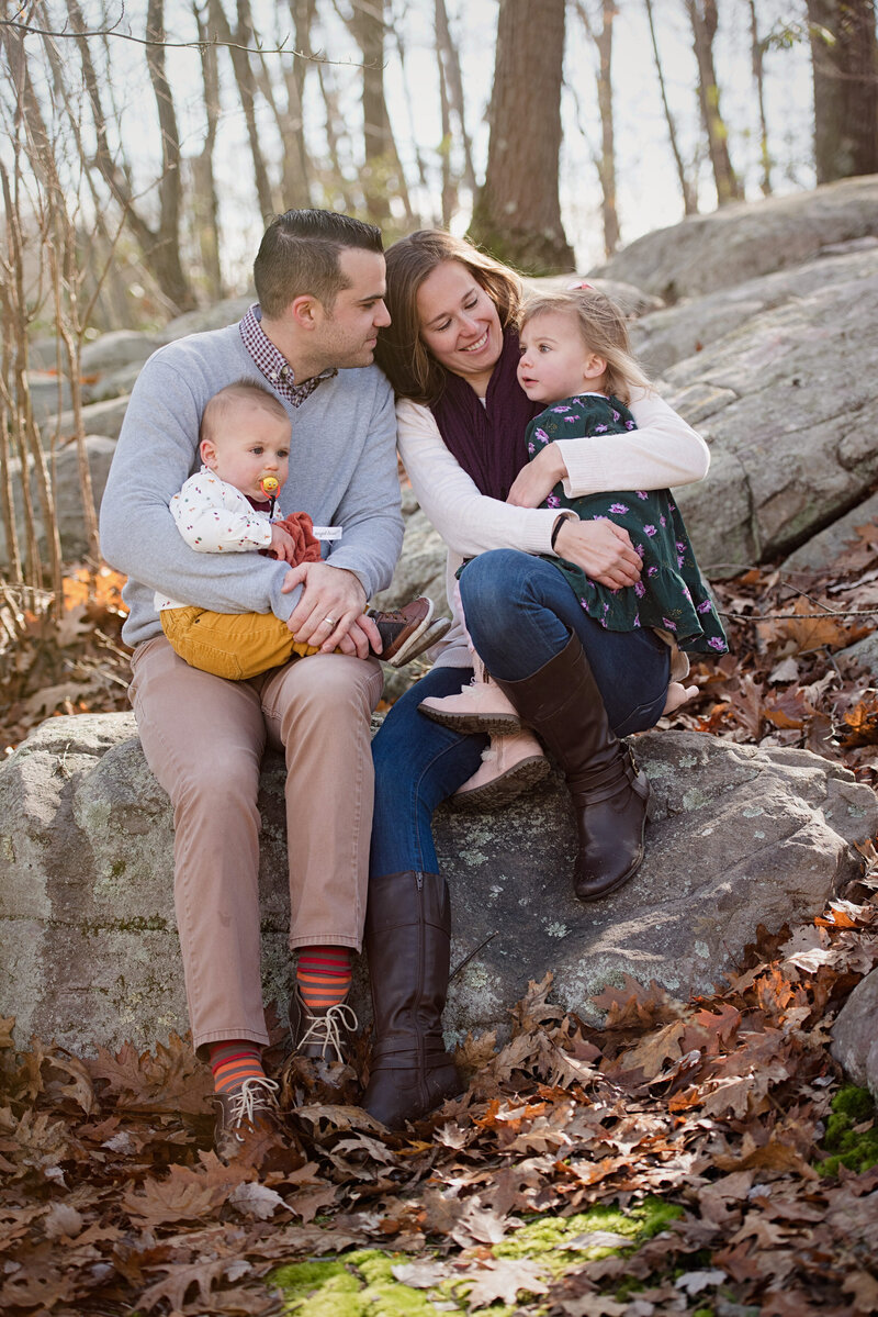 Two parents sitting on a rock each holding a child